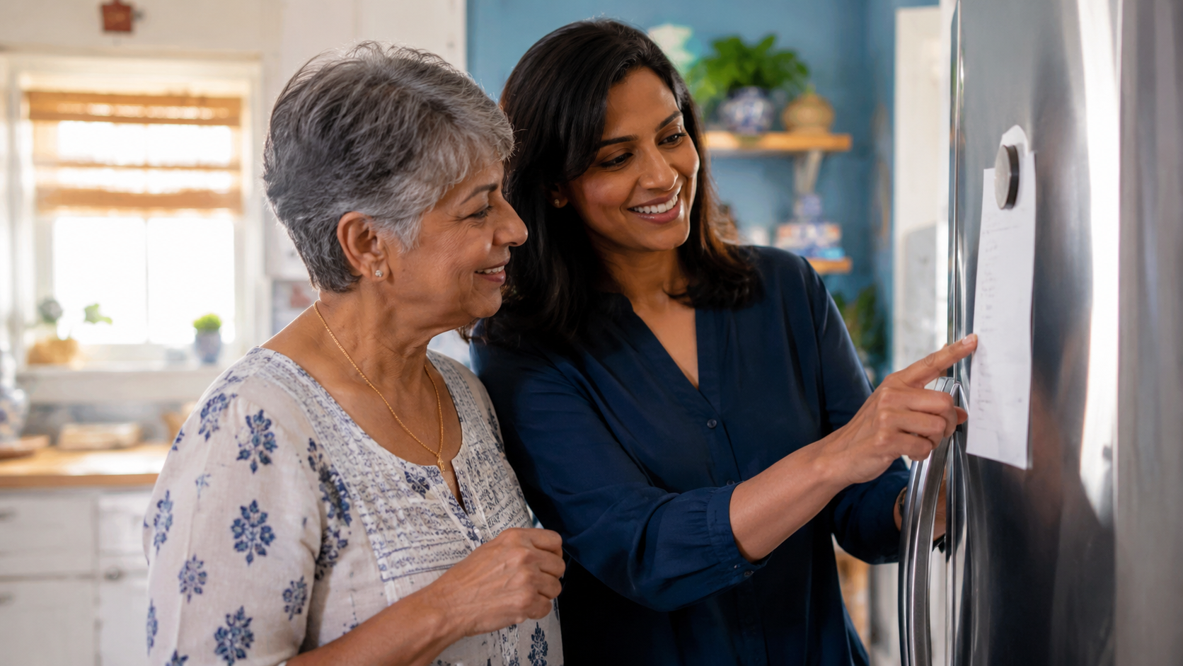 Smiling senior woman and her adult daughter looking at a weekly checklist posted on the refrigerator in a bright kitchen